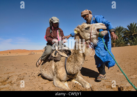 Ein Berber hilft ein Tourist auf einem Kamelritt in der Sahara in der Nähe von Merzouga, Erg Chebbi, Marokko Stockfoto