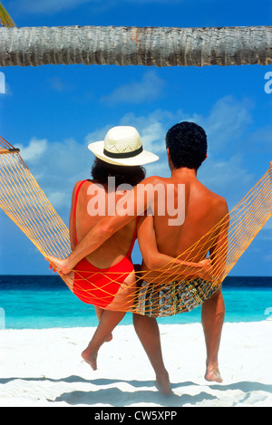 Paar sitzen zusammen in der Hängematte unter Palmen und blauem Himmel über weißen Sandstrand auf den Malediven Stockfoto