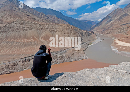 Ein Mann sitzt auf einem Aussichtspunkt Blick auf die verschiedenen farbigen Wasser des Flusses Zanskar & Indus in Ladakh, Indien Stockfoto