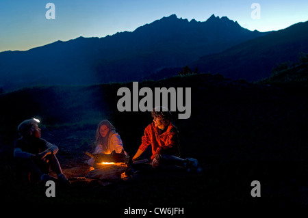 Lagerfeuer in den Bergen. Drei Kinder sitzen um ein Feuer in den Alpen, Frankreich Stockfoto