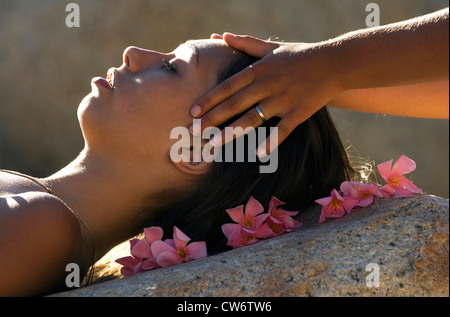 junge Frau immer eine Kopfmassage liegend mit dem Kopf auf einer Steinplatte und umgeben von rosa Blüten, Frankreich Stockfoto