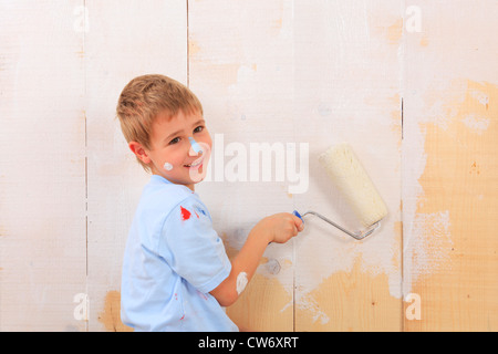 junge Malerei eine Holzwand weiß mit einem Farbroller Stockfoto