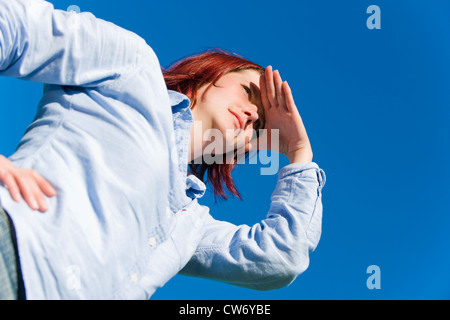 Würmer-Blick auf eine rothaarige junge Frau vor blauem Himmel mit einer Hand Schattierung die Augen schauen Stockfoto