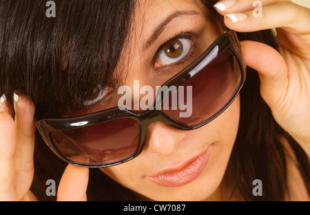 Brünette junge Frau, die über ihre Sonnenbrille Stockfoto