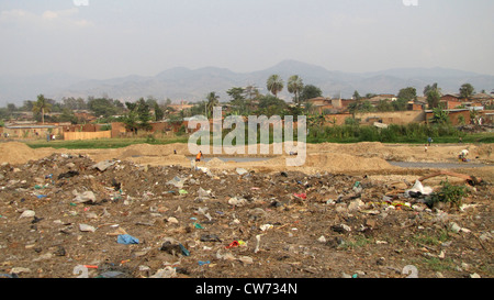 Frauen Waschen von Kleidern und Männer Schaufeln Sand in Eimer an einen Fluss mit Müll bedeckt; im Hintergrund die Elendsviertel der Hauptstadt Burundis, Bujumbura Mairie, Buyenzi, Bujumbura Stockfoto