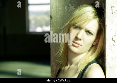 blonde junge Frau lehnt sich an die Wand der Fabrikhalle, Porträt, Deutschland Stockfoto