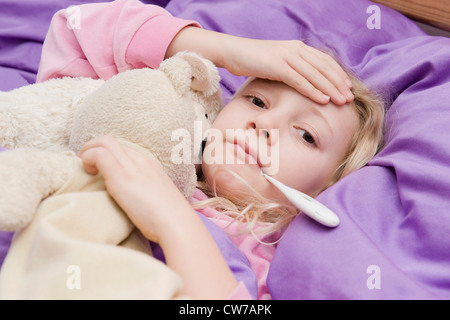 krankes Mädchen mit Fieberthermometer im Bett Stockfoto
