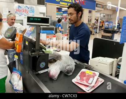 Lächelnde junge Hispanic männlichen Kasse klingelt Produkte für Kunden auf ein Wal-Mart Supercenter in San Marcos, Texas Stockfoto