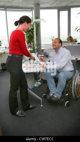 Mann im Rollstuhl an einem PC arbeiten und im Gespräch mit einer Frau Stockfoto