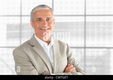 Porträt von einem mittleren Alter Geschäftsmann vor Bürofenster. Mann lächelt und verschränkten Armen hat. Querformat. Stockfoto