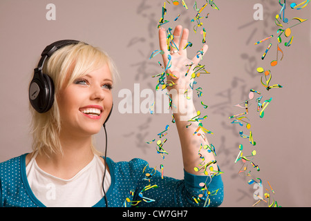 Blonde Frau mit Kopfhörern mit farbigen Noten um sie herum Stockfoto