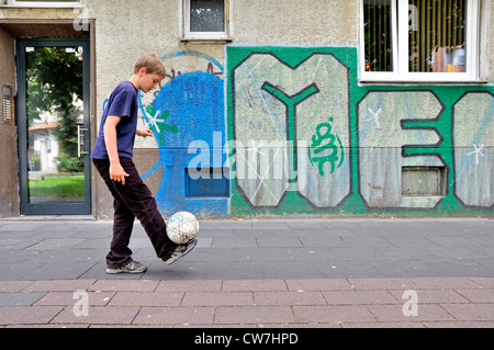 zehn Jahre alten Jungen spielen Fußball auf der Straße, Deutschland Stockfoto