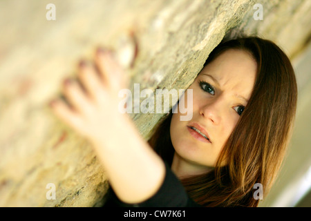 junge Frau mit langen braunen Haaren, die an eine Wand gelehnt Stockfoto