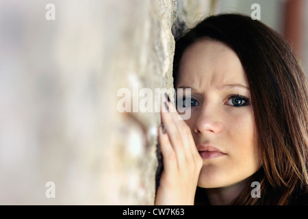 junge Frau mit langen braunen Haaren, die an eine Wand gelehnt Stockfoto