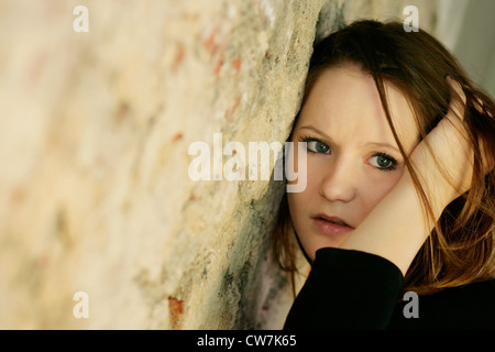 junge Frau mit langen braunen Haaren, die an eine Wand gelehnt Stockfoto