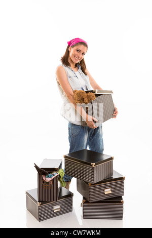 Fröhliche junge Dame Blick in die Kamera, hält eine gestreifte Kiste, in der Nähe von einem Stapel von Kisten. Stockfoto