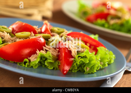 Frischer Thunfisch, Tomaten und grünen Oliven Salat serviert auf Salatblatt auf blauen Teller mit der Gabel auf der Seite Stockfoto