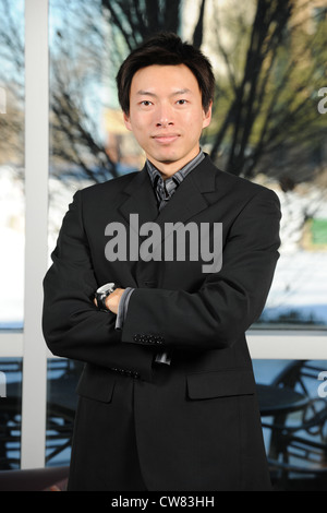 Junge asiatische Geschäftsmann mit verschränkten innerhalb eines Bürogebäudes Stockfoto