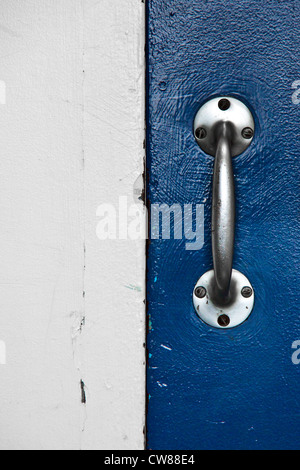 Inox Stahl Griff mit 6 Schrauben an einer blauen Tür halb rechts auf das Bild fixiert. In der anderen Hälfte ein weißes Holz Stockfoto