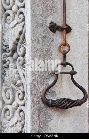 Alte schmiedeeiserne Glocke Griff, rostig und mit entblätterte Farbe an der Wand befestigt. Auf der linken Seite hat die Wand eine basorelief Stockfoto