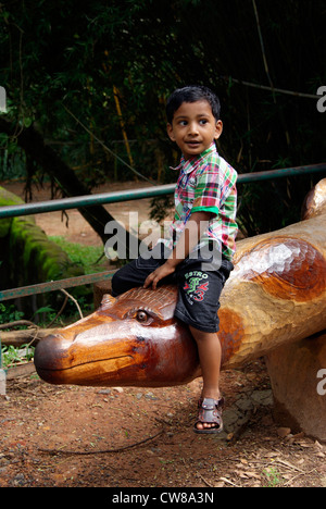 Kleiner Junge genießt sitzen auf der Krokodil geformten Holzbank im Zoo von Trivandrum in Kerala in Indien Stockfoto