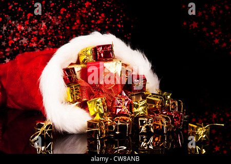 Weihnachtsgeschenke fallen aus der Weihnachtsmütze auf schwarzem Hintergrund Stockfoto