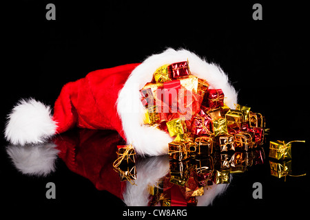 Weihnachtsgeschenke fallen aus der Weihnachtsmütze auf schwarzem Hintergrund Stockfoto