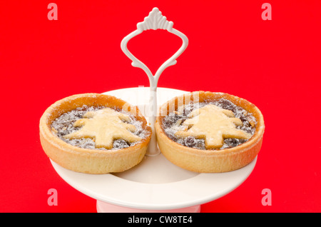 Festliche oder Weihnachten Mince Pies frisch gemacht und auf einen Kuchenteller - Studio gedreht mit einem roten Hintergrund platziert Stockfoto