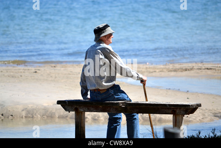 Alter Mann sitzt auf der Bank mit Blick auf Meer Stockfoto