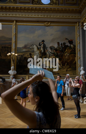 Touristen hören Sie Audio-Führungen und verwenden Kameras und Smartphones zu Rekord Kunstwerke unter ein Gemälde von Napoleon in der Schlacht von Wagram, hängen in der Halle Schlachten in des Königs Wohnungen der Palast von Versailles, Paris. Die Schlacht von Wagram (5 – 6 Juli 1809) gehörte zu den wichtigsten militärischen Engagements der napoleonischen Kriege und endete mit einem entscheidenden Sieg für Kaiser Napoleon i's französische und Verbündete Armee gegen die Österreicher. "Napoleon am Wagram" wurde von Horace Vernet (Galerie des Batailles, Versailles) gemalt. Stockfoto