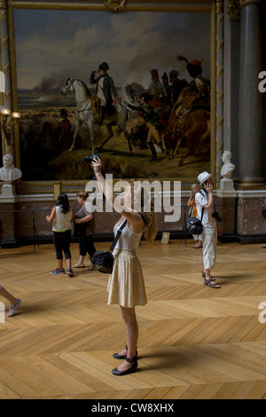 Touristen hören Sie Audio-Führungen und verwenden Kameras aufzeichnen Kunstwerke unter ein Gemälde von Napoleon in der Schlacht von Wagram, hängen in der Halle Schlachten in des Königs Wohnungen der Palast von Versailles, Paris. Die Schlacht von Wagram (5 – 6 Juli 1809) gehörte zu den wichtigsten militärischen Engagements der napoleonischen Kriege und endete mit einem entscheidenden Sieg für Kaiser Napoleon i's französische und Verbündete Armee gegen die Österreicher. "Napoleon am Wagram" wurde von Horace Vernet (Galerie des Batailles, Versailles) gemalt. Stockfoto