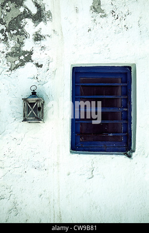 eine hölzerne Laterne hängt an einer weißen Wand neben einem blauen Fenster Stockfoto