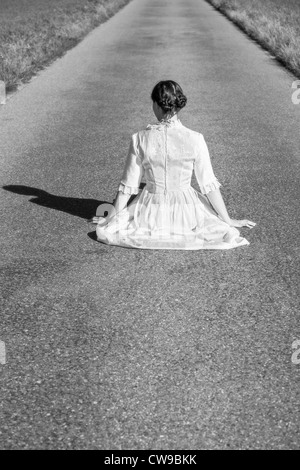 eine Frau in einem viktorianischen Kleid sitzt auf der Straße Stockfoto