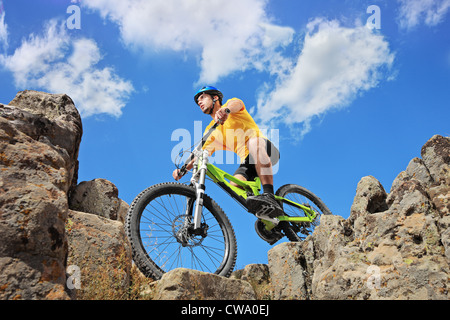 Person auf einem Mountainbike inmitten von Felsen an einem sonnigen Tag gegen einen blauen Himmel und Wolken, niedrigen Winkel anzeigen Stockfoto