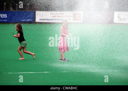 Kinder spielen unter der Wassersprenger an einem heißen Sommertag im Masters-Hockey-Weltmeisterschaft, Canterbury, Kent. Stockfoto