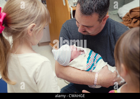 Vater wiegt neugeborenes Mädchen mit zwei älteren Schwestern Stockfoto
