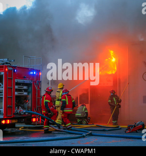 Feuerwehr in Aktion Flammen sprühen. Auto-Werkstatt in Brand in einem Vorort von Reykjavík, Island Stockfoto