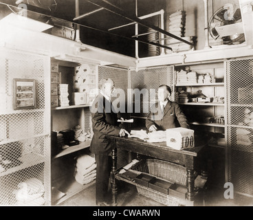 Zwei Männer im Tresor in der Treasury-Abteilung für tägliche Betriebsmittel.  Auf dem Tisch liegen Säcke Münze, Bündel von Rechnungen und einer Stockfoto