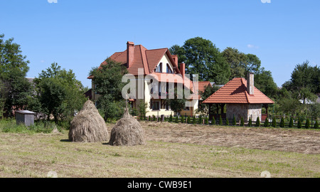 Heu-Feld mit Ballen auf Vordergrund Bauernhaus im Hintergrund Stockfoto