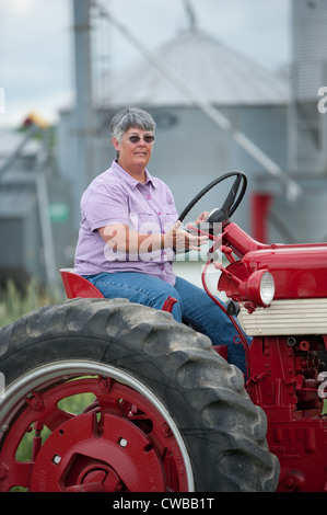 Frau Bauer Reiten Traktor vor Ackerland vor Scheunen und silos Stockfoto