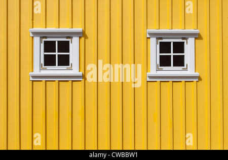 Leuchtend gelbe Holzwand mit zwei kleinen Fenstern Stockfoto