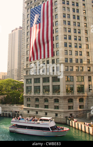 Ein Ausflugsschiff Wendella verlässt das Dock auf dem Chicago River wie eine amerikanische Flagge unten vom Wrigley Gebäude in der Innenstadt von hängt Stockfoto