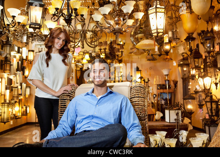 Porträt von gut aussehenden jungen Mann sitzend und Frau stehend Hintergrund im Leuchten Shop Stockfoto