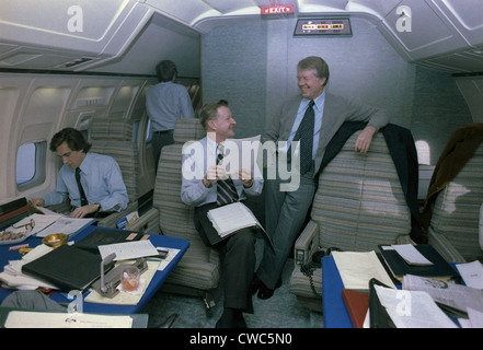 Zbigniew Brzezinski und Jimmy Carter in einem entspannten Gespräch an Bord der Air Force One, während eine junge Mitarbeiterin inmitten Papiere in arbeitet Stockfoto