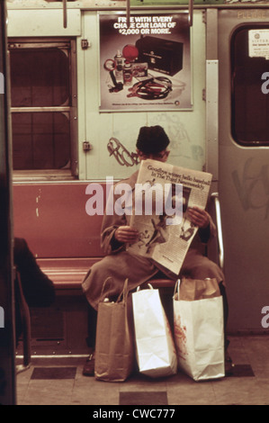 New York City Subway. Ein Passagier ist in seiner eigenen Welt mit seinem Einkaufstüten sicherte sich zwischen seinen Füßen seine Zeitung lesen. Stockfoto