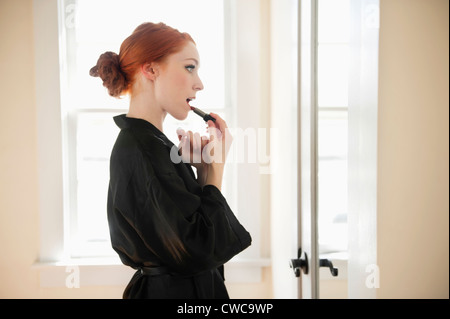 Höhenplan einer jungen Frau in Robe Auftragen von Lippenstift Stockfoto
