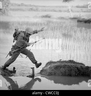 Vietnam-Krieg. Ein US-Marine Schütze Sprünge über eine Pause in einem Reisfeld Deich bei einer Durchsuchung and destroy-Mission Operation Stockfoto