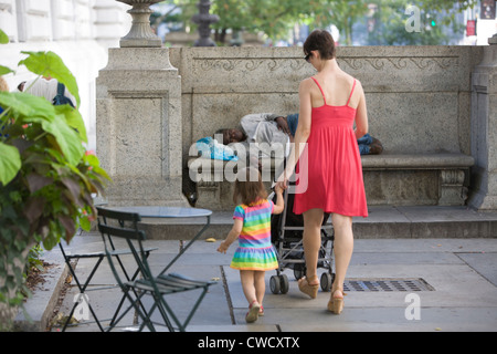 Mutter und Tochter gehen an einer obdachlosen Frau vorbei, die sich auf dem Gelände der NY Public Library in der 42nd St. & 5th Ave. In NYC ausruhen. Stockfoto