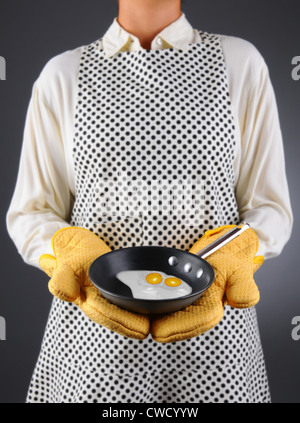 Nahaufnahme einer Hausfrau in eine Schürze und Backofen Handschuhe halten eine Pfanne mit zwei Spiegeleiern. Stockfoto