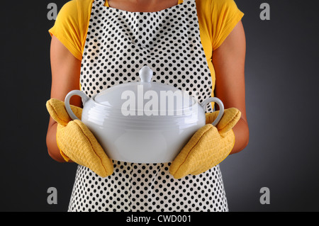 Nahaufnahme einer Frau in einer Schürze und Backofen Handschuhe halten eine Suppenschüssel. Frau ist nicht erkennbar. Stockfoto
